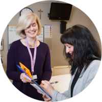 A female social worker holds out a clipboard to a women, who signs some paper work. 